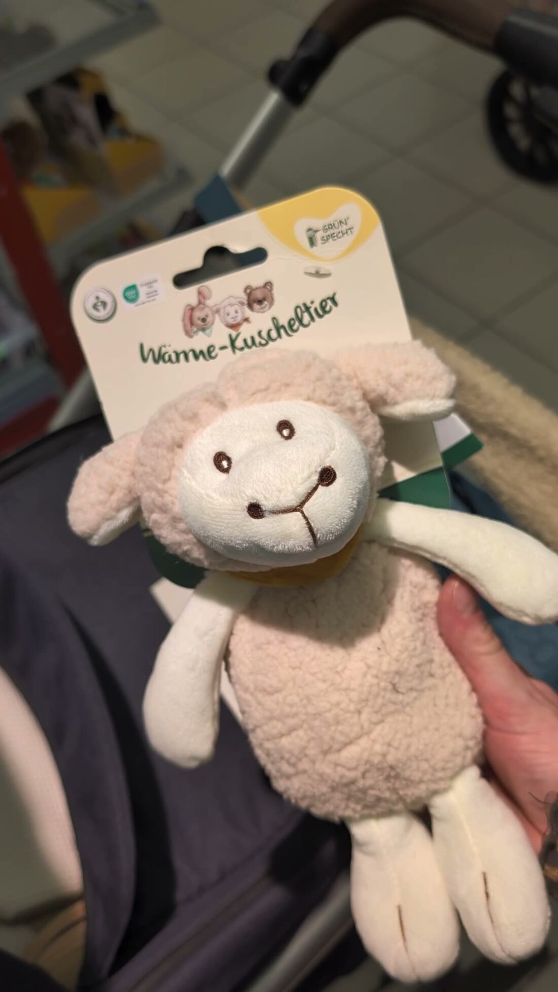 Ein Wärmekissen in Schaf-Form in der Verpackung, in der Hand gehalten.